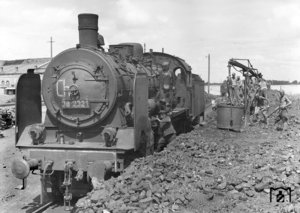 38 2321 im Bw Cherson (Ukraine). Bei der Bekohlung ist Handarbeit gefragt, während der Heizer zwischen Kohlenbergen und Dreck an der Maschine Reparaturarbeiten ausführt. (1942) Foto: RVM (Ittenbach)